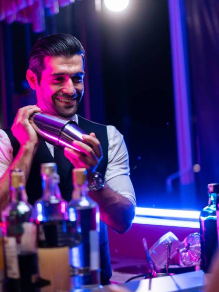 Caucasian profession bartender making a cocktail for women at a bar. Attractive barman pouring mixes liquor ingredients cocktail drink from cocktail shaker into the glass at night club restaurant.